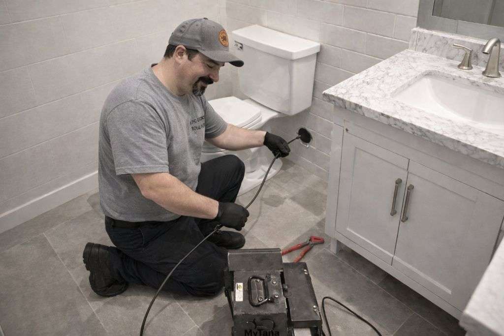 Plumber Jerry running a camera in a drain pipe in wall behind toilet